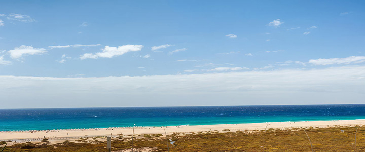 Weitläufiger, weißer Sandstrand vor tiefblauem Meer unter einem strahlend blauen Himmel – ideales Postkartenmotiv für einen Badeurlaub.